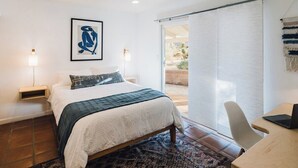 A bedroom with a bed, bedside lamps, a desk with a laptop, a framed artwork, and a sliding door to a patio. - Top 1% | 4min->JTNP+Town|Cinema|Hot Tub|Fire Pit (Joshua Tree)