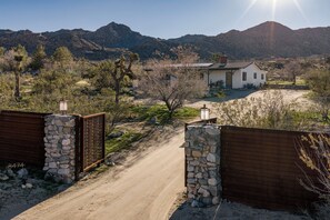 A rural road leading to a house with a stone wall and wooden gate.