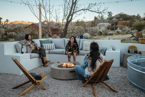 A cozy outdoor seating area with a fire pit, a sofa, and two chairs.