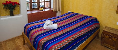 A bed with a colorful striped bedspread, a window with a view of a fence, and a vase with red flowers on the windowsill.