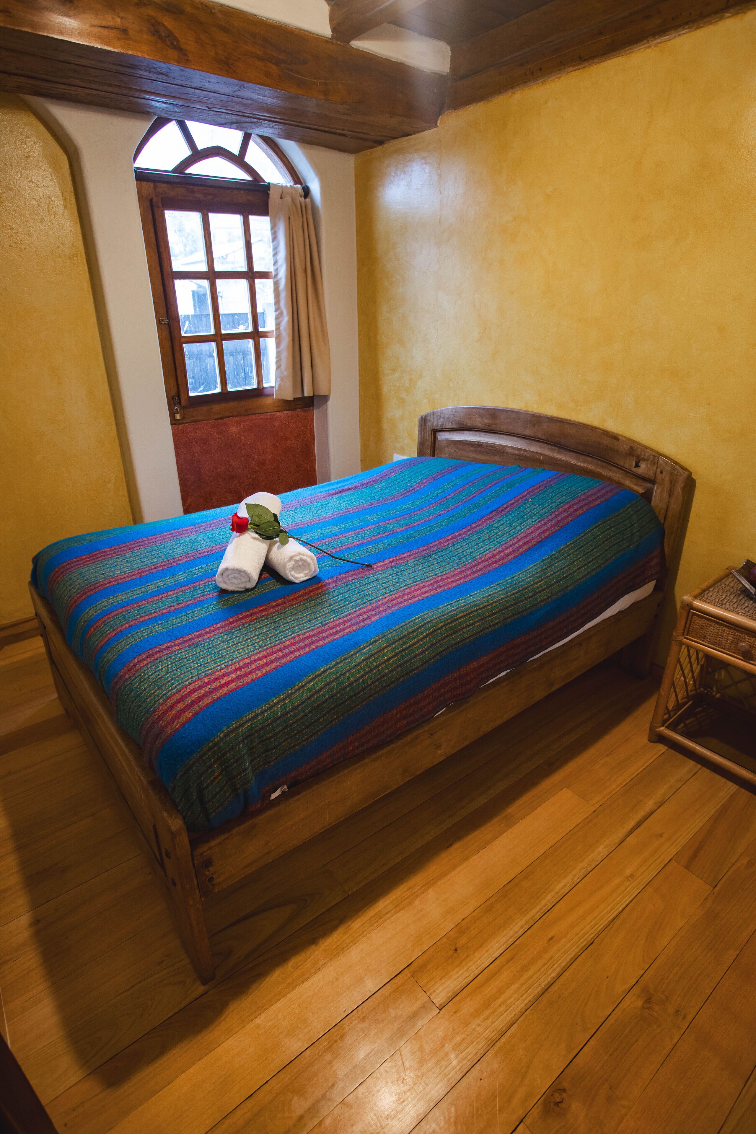 A wooden bed with a colorful striped bedspread and rolled towels with a rose.