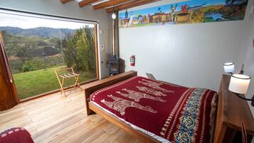 Un dormitorio con una cama grande, suelo de madera, vistas al exterior, chimenea y un cuadro en la pared.