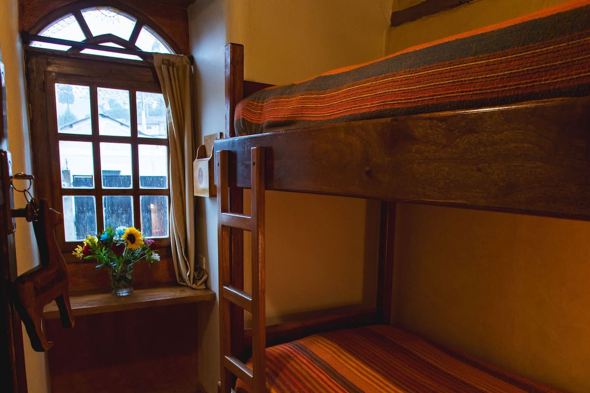 Habitación con literas, suelo de madera y ventana con cortinas.