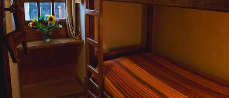 A bunk bed room with wooden floors and a window with curtains.