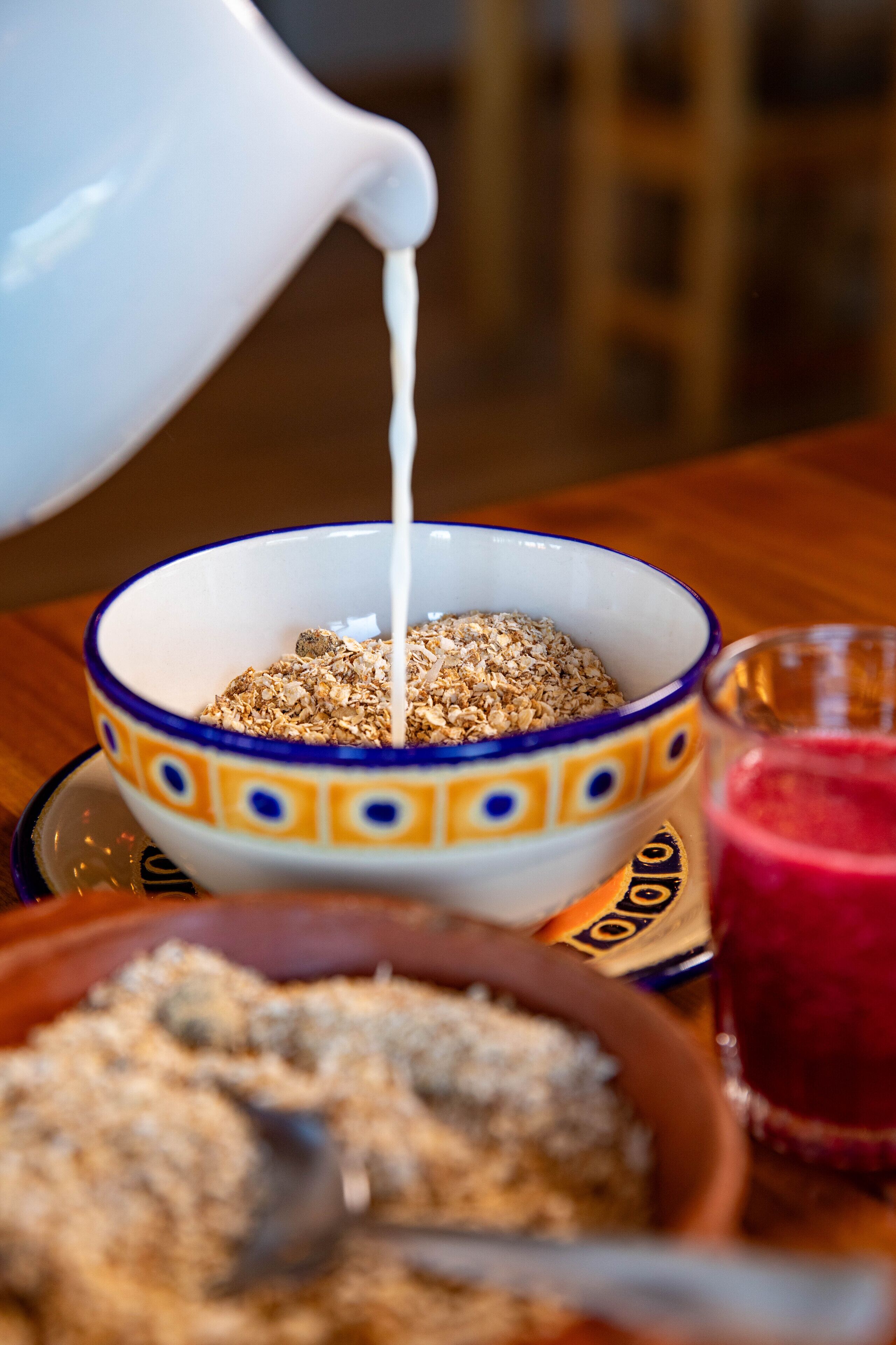 Eine Schüssel mit Cornflakes und Milch, ein Glas roter Saft und eine Schüssel Granola auf einem Tisch.