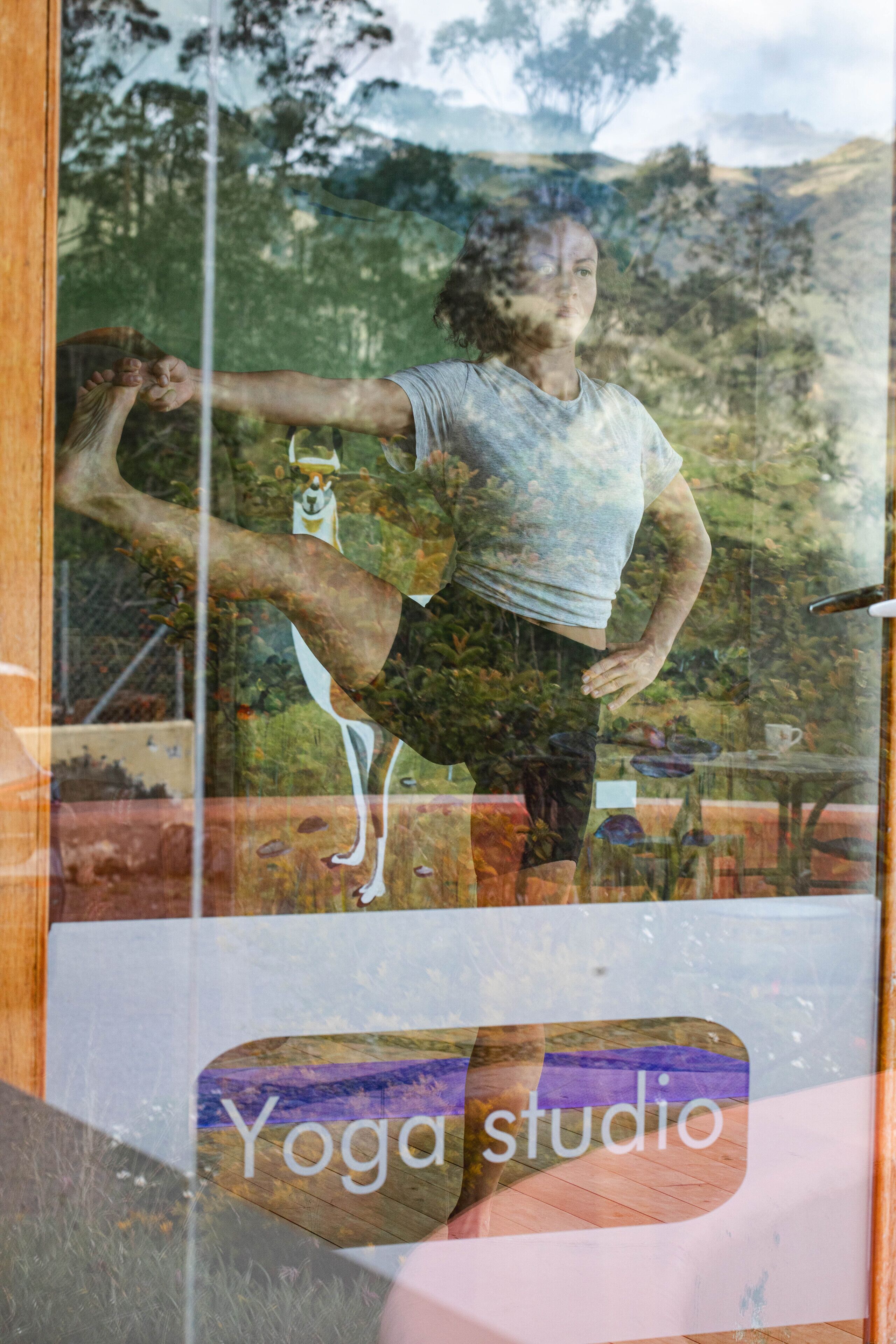 Un estudio de yoga con una pared de vidrio que refleja a alguien realizando una postura de yoga.