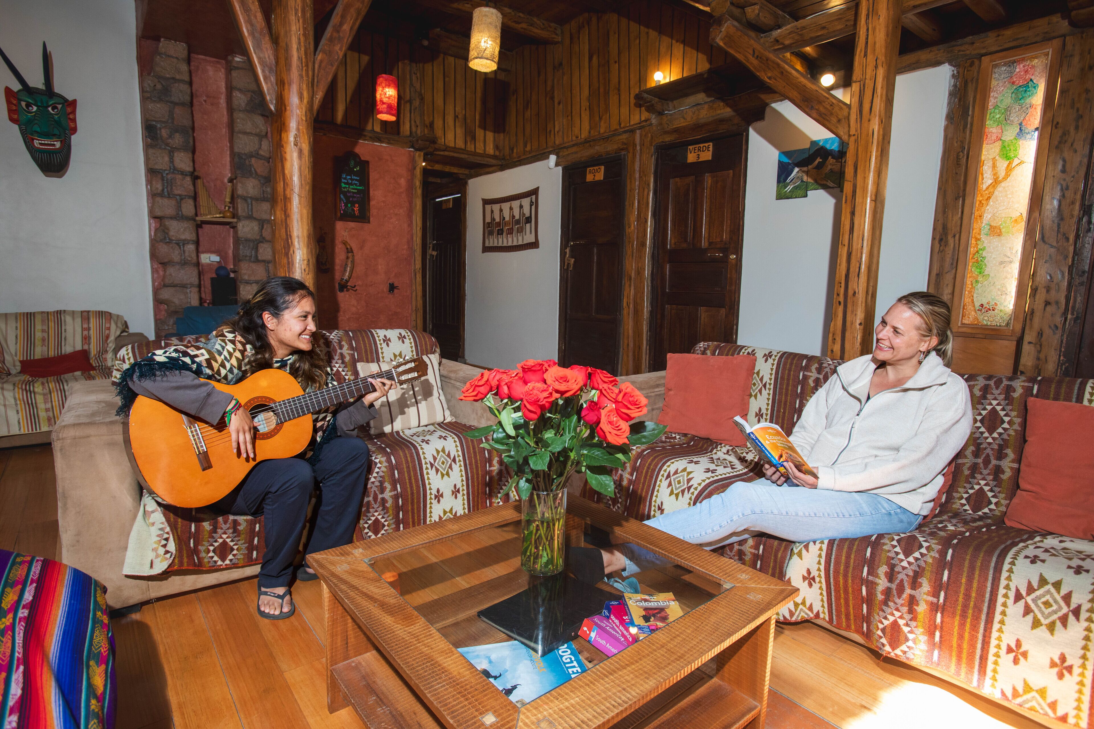 Una sala de estar acogedora con techo de madera, una mesa de centro con un jarrón de rosas rojas y una guitarra sobre un sofá.