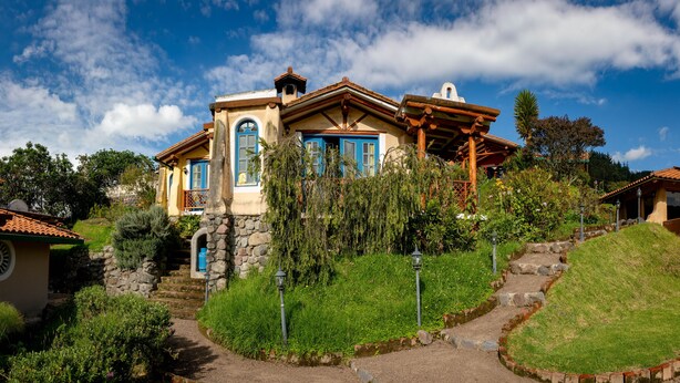 Ein zweistöckiges Haus mit Naturstein-Fassade, blauen Fensterläden und einer Holzveranda.