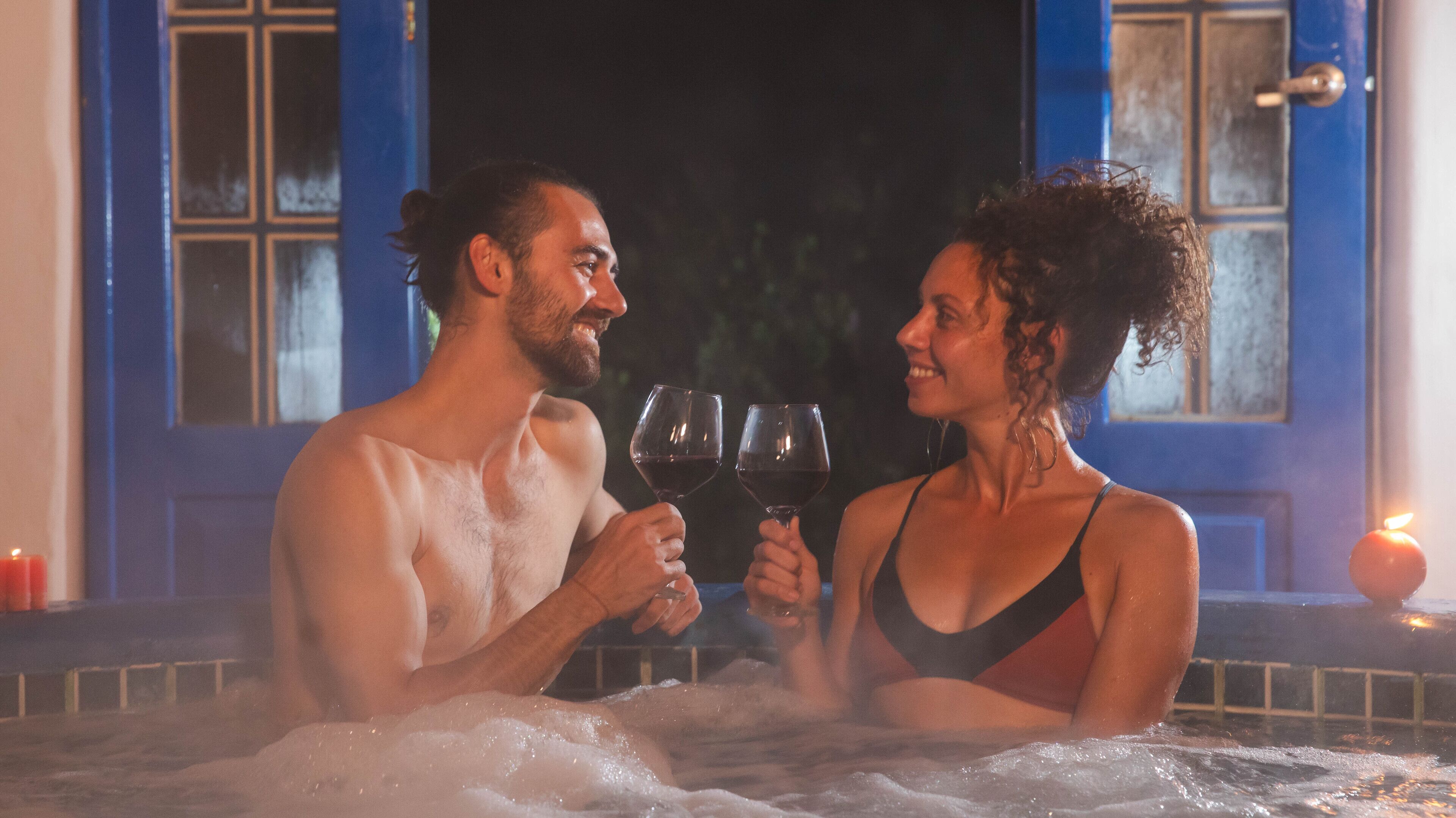 Ein Paar in einer Badewanne, mit Kerze und einer weiteren angezündeten Kerze daneben.