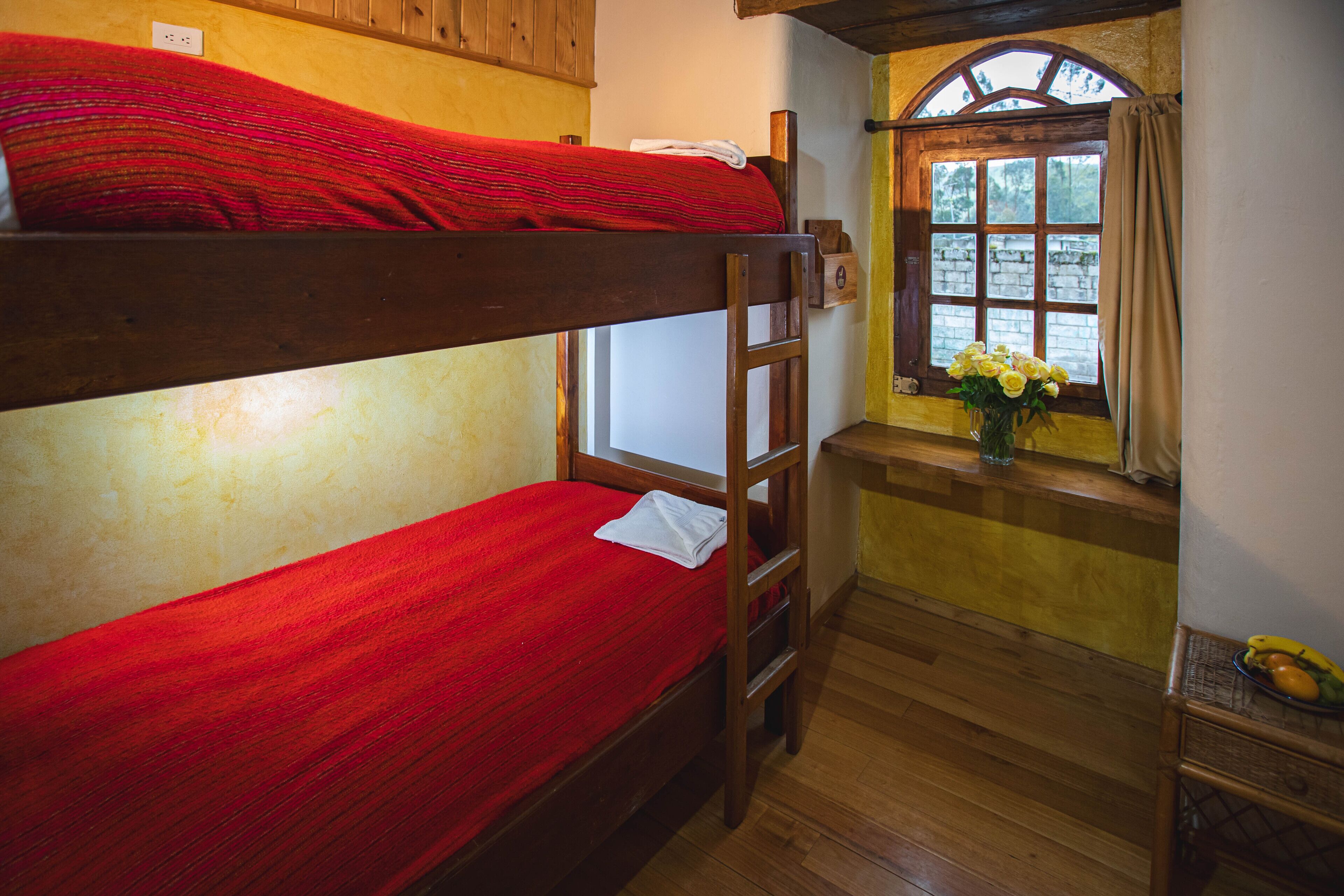 A bunk bed room with a wooden ladder, a window with a view, and a small table with a vase of flowers.