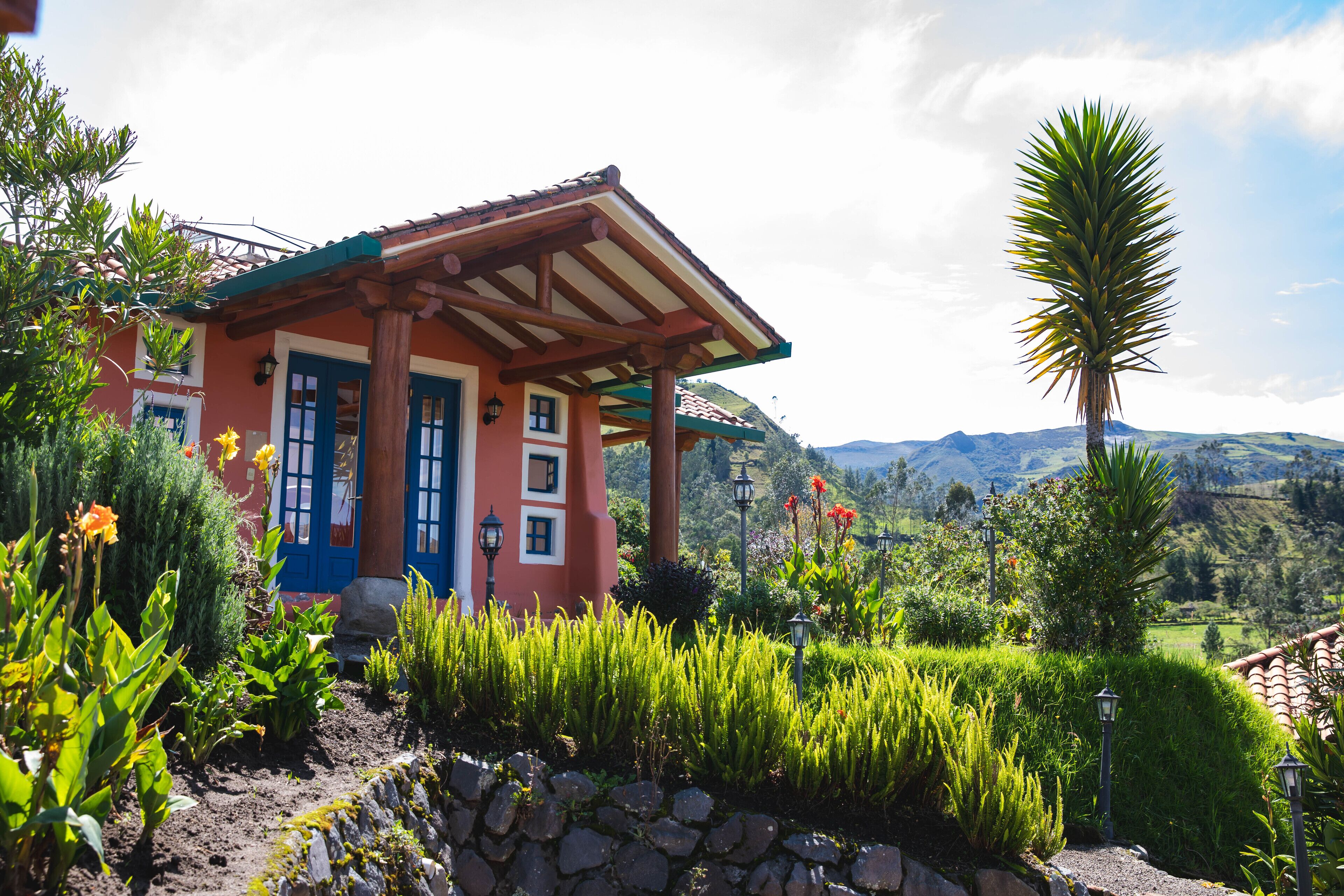 A house with a red facade, blue doors, and a stone pathway leading to it.