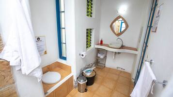 Un baño con inodoro, lavamanos, espejo y cubo de basura.