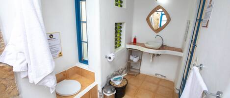 A bathroom with a toilet, sink, mirror, and a trash bin.