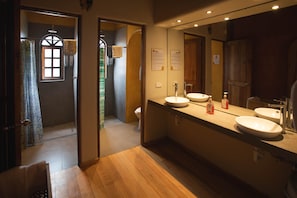 A modern bathroom with wooden flooring, a large mirror, two sinks, and a shower area.