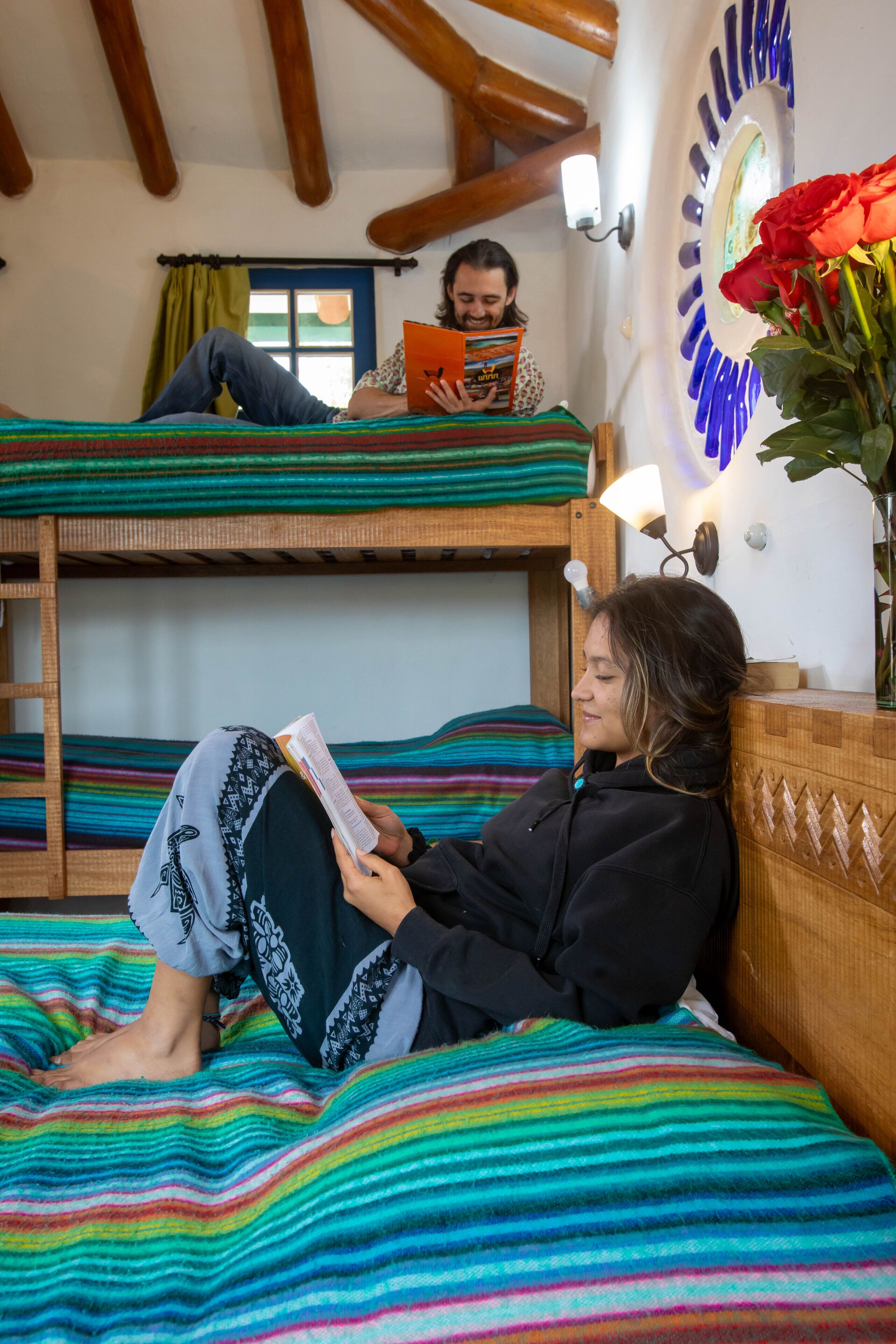 Una habitación con literas, una lámpara de lectura y un jarrón con una flor.
