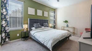 Une chambre à coucher comprenant un lit, une table de chevet, une commode, un ventilateur de plafond et un bureau avec une chaise.