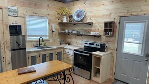 Una cucina compatta con mobili in legno, un frigorifero in acciaio inossidabile, un piano cottura e un lavello. Sono presenti sgabelli da bar e un piccolo tavolo.