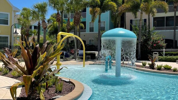 Ein Pool mit einer Wasserspeier, umgeben von Palmen und einem Gebäude mit Balkonen.