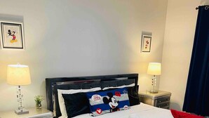 Ein ordentlich bezogenes Bett mit einem Mickey Mouse Kissen, zwei Nachttische mit Lampen und ein Holzboden.