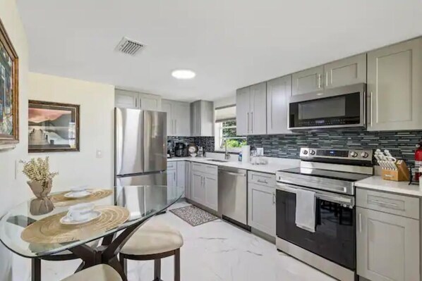 A modern kitchen with stainless steel appliances, a glass dining table, and light-colored cabinetry.