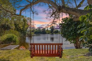 A wooden swing bench overlooking a calm lake with a sunset in the background.