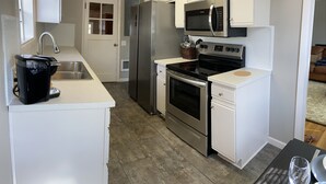 A modern kitchen with white cabinets, stainless steel appliances, a microwave, oven, and a sink. - Cozy 2 br. Close to River (Milwaukie)