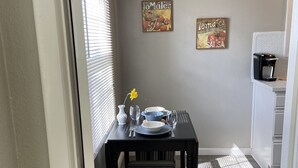 A dining area with a table set for two, a striped bench, and two wall decorations. - Cozy 2 br. Close to River (Milwaukie)