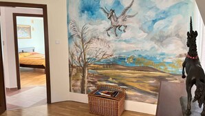 A room with a large mural of a horse and rider, a wicker basket with books, and a bed with a yellow blanket. - Holiday home right on the bank with a view (Balatonboglár)