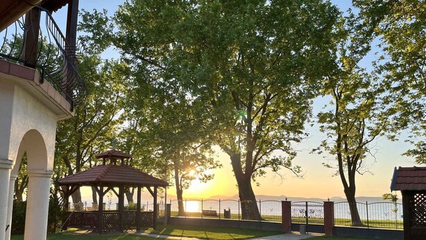 A gazebo in a park with a view of the sunset over a body of water. - Holiday home right on the bank with a view (Balatonboglár)