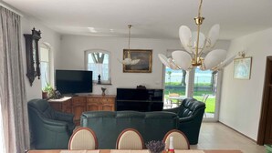 A dining area with a wooden table set for four, a green sofa, and a television in the background. - Holiday home right on the bank with a view (Balatonboglár)