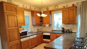 A kitchen with wooden cabinets, a central island, a dishwasher, an oven, and a coffee maker. - Holiday home right on the bank with a view (Balatonboglár)
