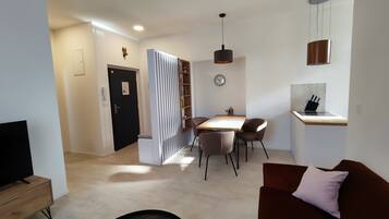 A modern living room with a sofa, a dining table with chairs, a TV, and a kitchen area with a sink and countertop.