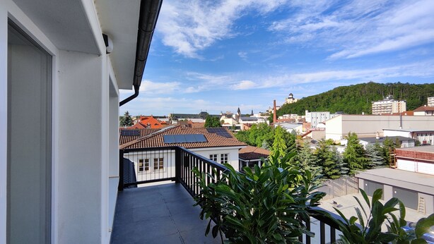 A balcony with a view of a town, including buildings and a hill with a tower. - DOHNANYI Villa by CHORS (Trencin)