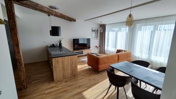 A modern living space with a wooden floor, a kitchen area with a black countertop, a sofa, and a dining table with chairs.