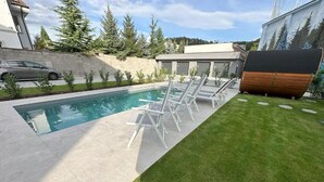 A modern outdoor pool area with a concrete deck, a grassy lawn, and a row of white lounge chairs. - DOHNANYI Villa by CHORS (Trencin)