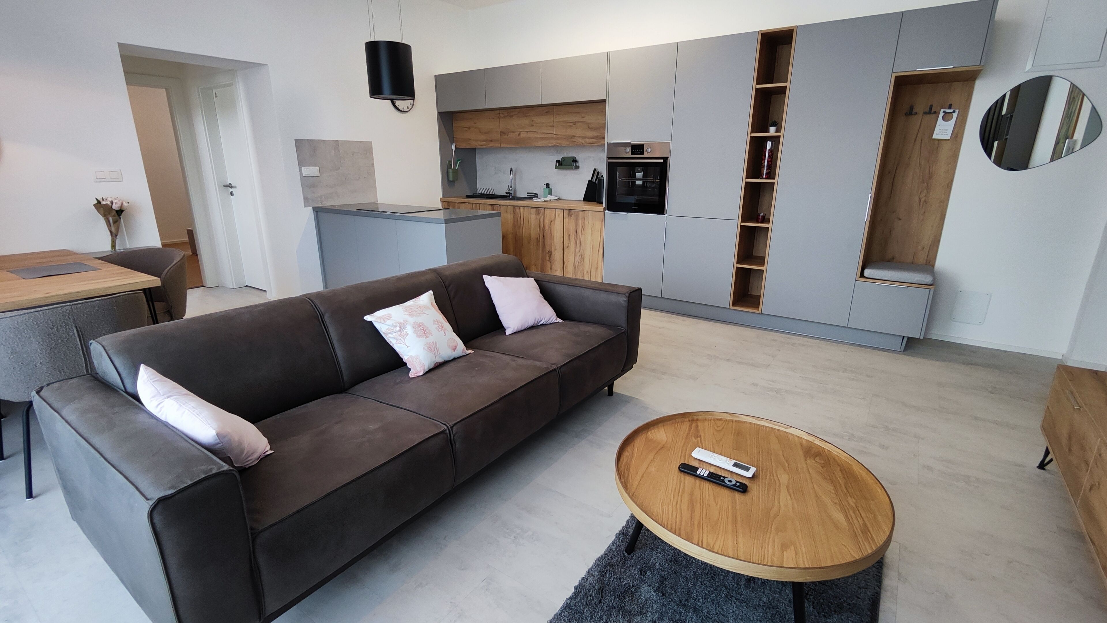 Ein modernes Wohnzimmer mit einem braunen Sofa, einem Holztisch und einer Küchenzeile mit grauen Schränken und einer Holz Arbeitsplatte.