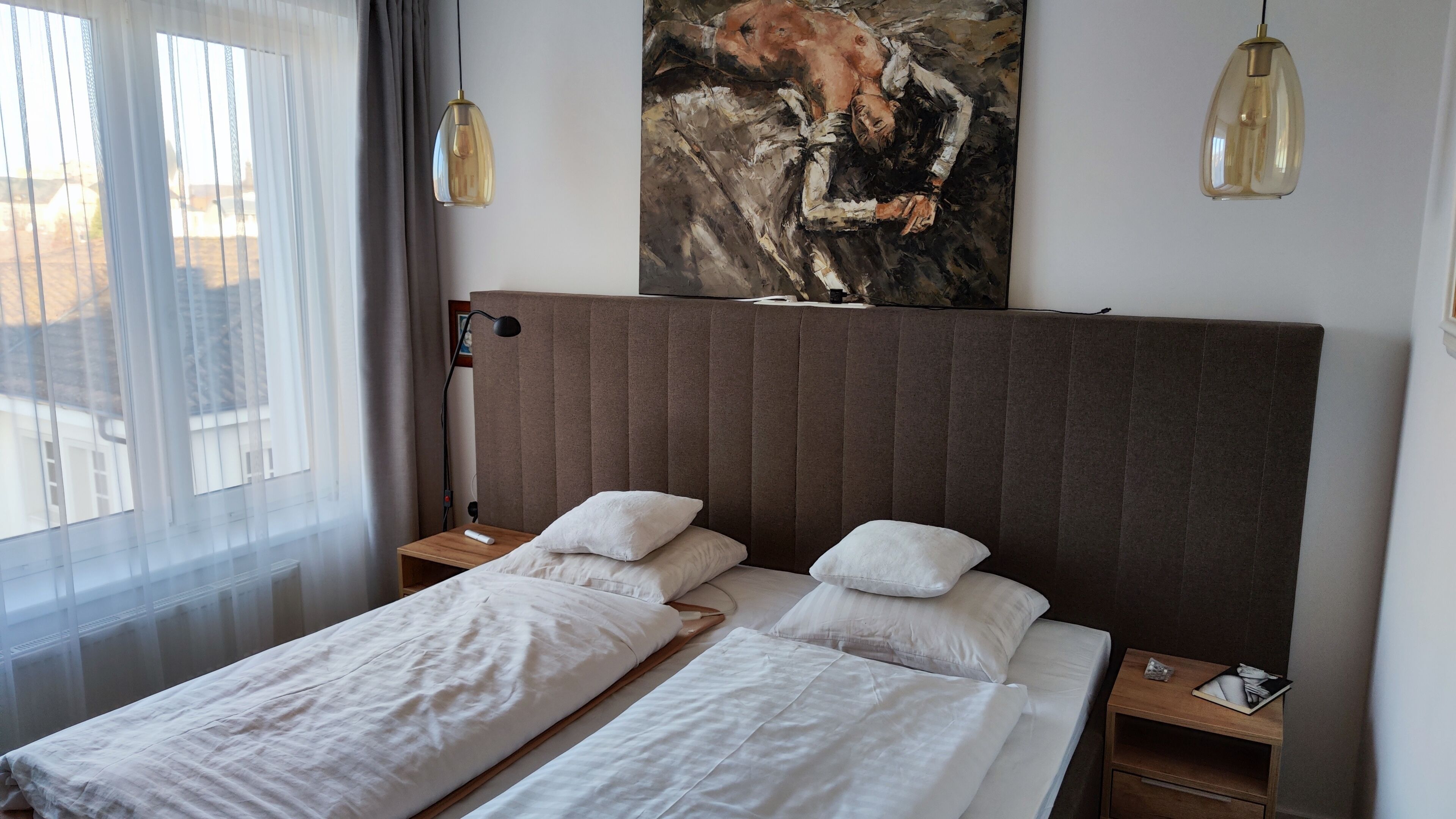 Una habitación de hotel con dos camas individuales, un cuadro grande en la pared y dos lámparas colgantes.