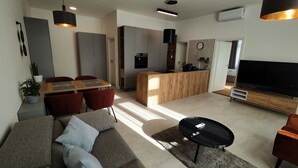 A modern living room with a sofa, a coffee table, and a TV. There is a kitchen area with a dining table and chairs. - DOHNANYI Villa by CHORS (Trencin)