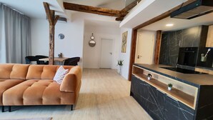 A modern living room with a sofa, a dining area with chairs, a kitchen with a black countertop, and a wooden ceiling beam. - DOHNANYI Villa by CHORS (Trencin)