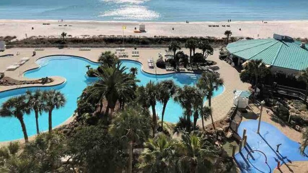 A resort with a large pool area, palm trees, and a beach view.