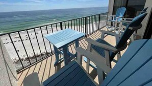 A balcony with a table and chairs, overlooking a beach with the ocean and a clear sky.