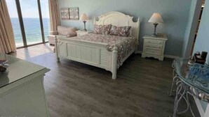 A bedroom with a large bed, two bedside tables, a dresser, and a view of the ocean.