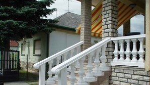 Un immeuble résidentiel avec un escalier blanc, un mur de briques et une entrée fermée par un portail.