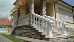 Une maison à deux étages avec une façade en pierre, un balcon doté de balustrades blanches et une antenne parabolique.