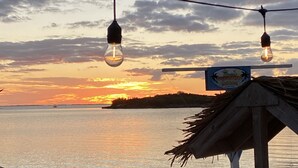 A beach scene with a wooden hut, a boat, and a signboard. - Private Oceanfront Home on the Bay of Great Guana Cay - Spectacular Views! (Great Guana Cay)