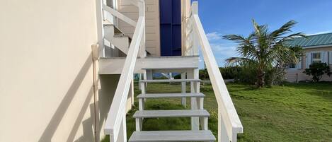 A white staircase leading to a blue door, surrounded by a grassy lawn and a clear blue sky.