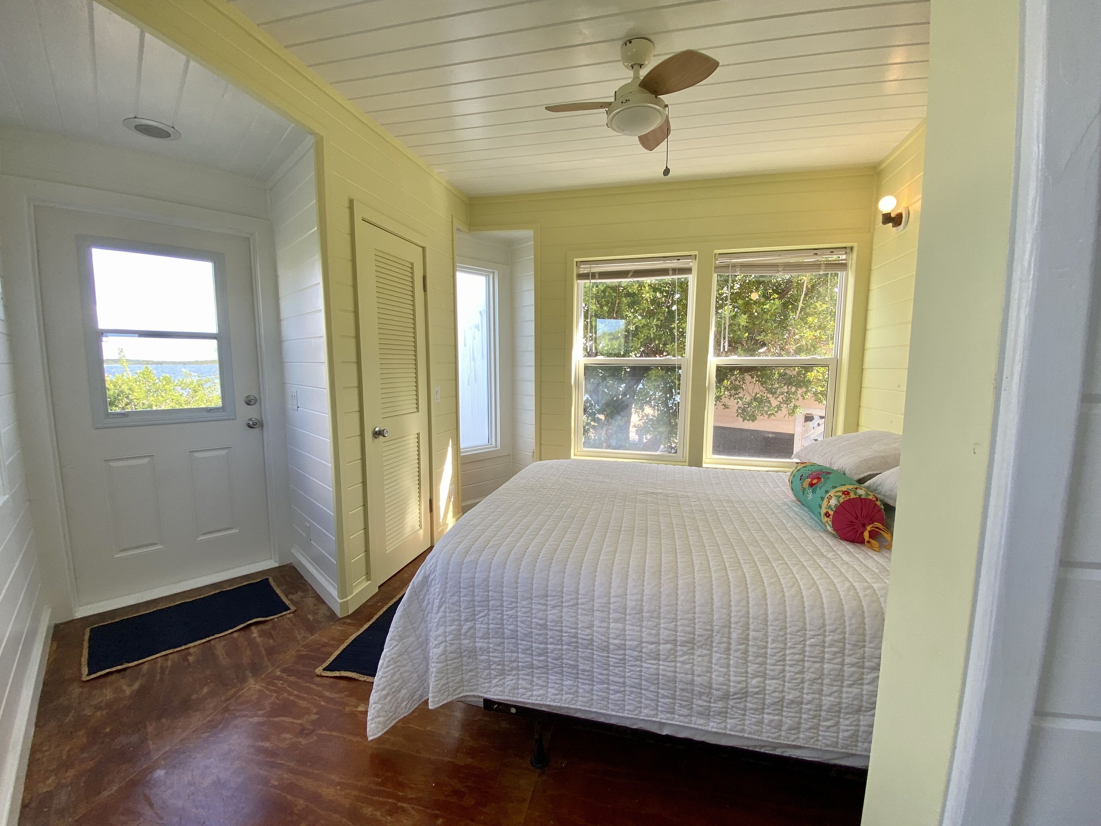 A bedroom with a bed, a ceiling fan, and two windows.