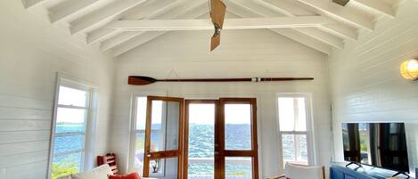 A spacious living room with a high ceiling, a large window, and a view of the sea.