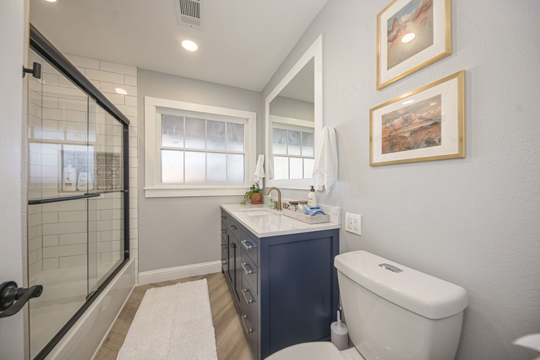 A bathroom with a glass shower enclosure, a white toilet, a vanity with a sink, and two framed pictures on the wall.