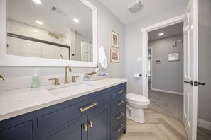 A modern bathroom with a large mirror, a white sink, and a dark blue vanity with gold handles. - Welcome to Twin Oaks Oasis (Midland)